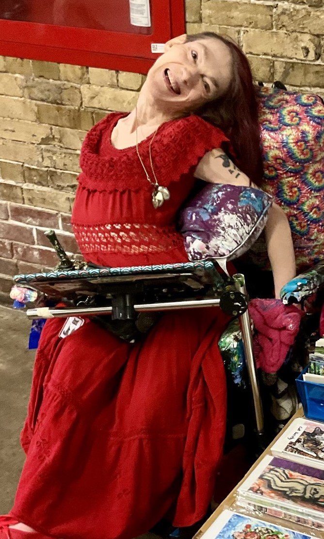 Anne, wearing an all-red outfit, smiles against a brick wall background.