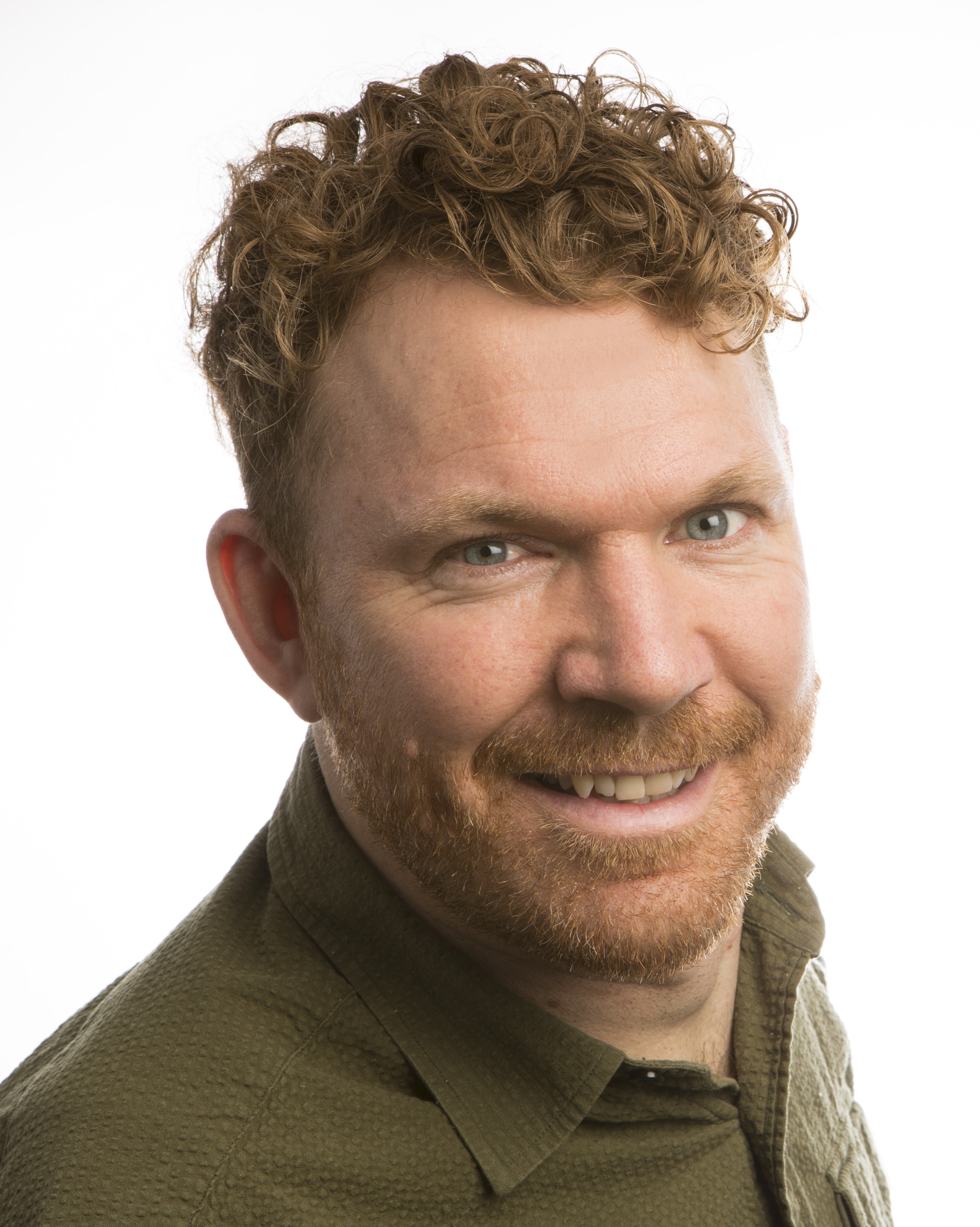 Headshot of Luke Anderson, who has short, curly, light brown hair and a short beard. He is wearing a moss-coloured shirt.